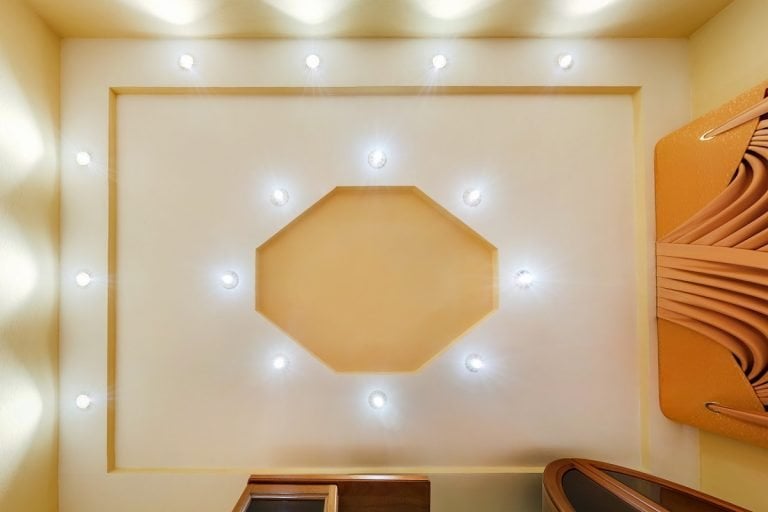 在公寓或房子的空房间里，白色和复杂形状的拉伸天花板，卤素斑点灯和石膏板结构。吊顶。天花板饰面类型。