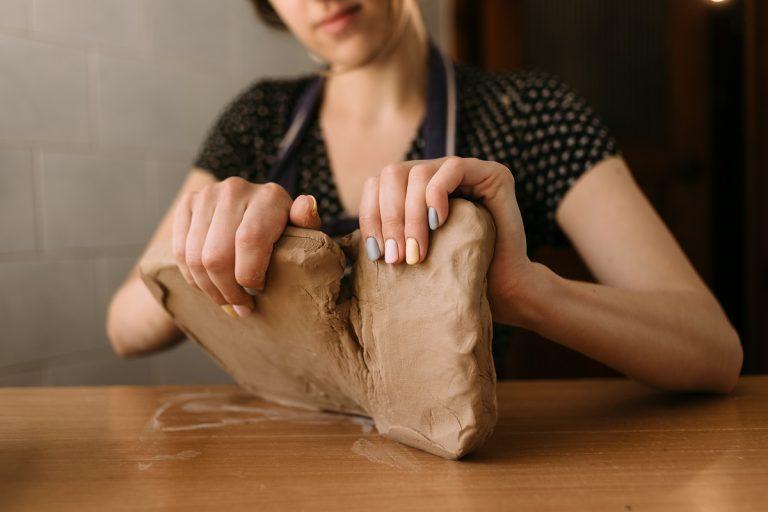 一个陶工的女性手的特写，开始用粘土制作产品，拿一大块材料，把它分成两部分。副本的空间。初学者雕刻粘土。